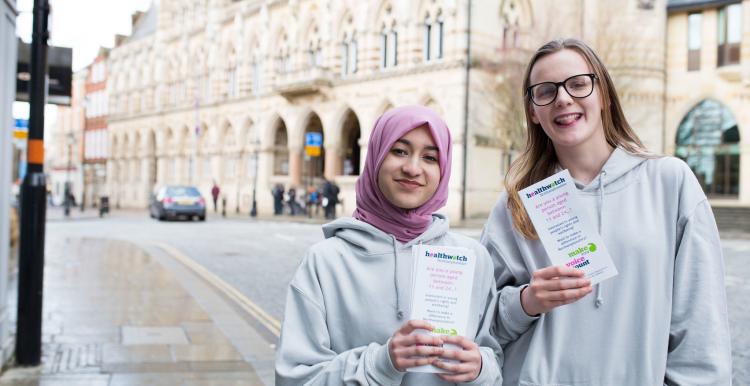 Two young teenagers holding up Healthwatch promotional material
