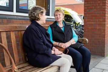 Two women talking on a bench outside a hospital