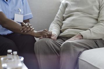 A nurse holding an old man's hand on the sofa.