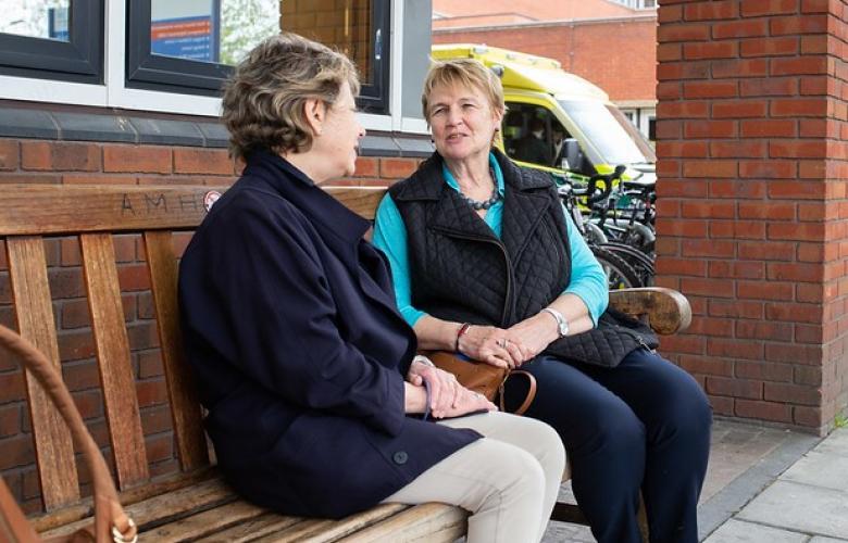 Two women talking on a bench outside a hospital